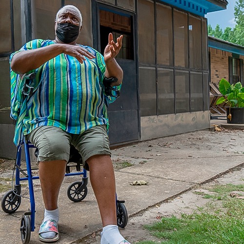 Person sitting on a walker while wearing a mask and speaking with their hands